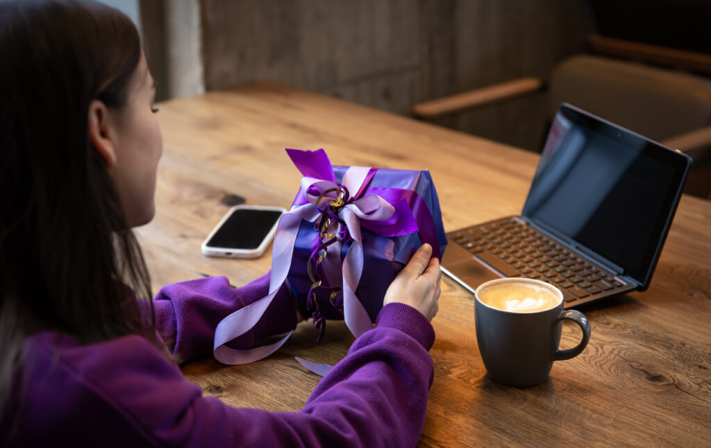 Purple gift box in a womans hands in a purple sweater - SastaOffer Experiences Gifts